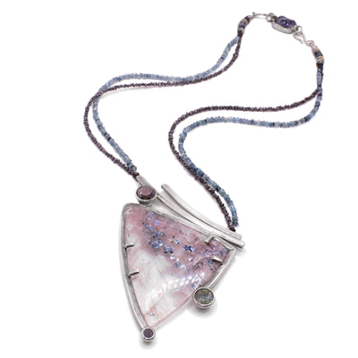 The lepidocrosite centerpiece of this gemstone necklace is triangular in shape with three circular gemstones attached at different sides. Silver accents hold the lepidocrosite in place. The necklace is made of two strands, one of sapphires and the other of black diamonds. At the back is a rectangular piece of sodalite.