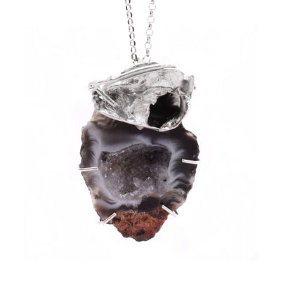 This agate necklace has a large, uniquely shaped piece of Ochoco agate with an abstract silver adornment on top. Crystals are visible on the inside of the agate. The agate is red, light grey, and dark grey in colour.