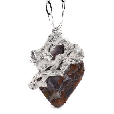 This jasper necklace has a diamond-shaped jasper encased in a large, abstract silver adornment on top to which the chain is attached to at the back. The jasper is purple, red, and grey in colour.