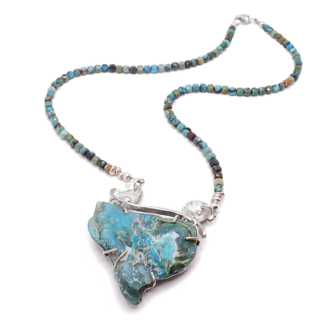 This chrysocolla necklace has a triangular-shaped light blue chrysocolla as the statement piece with silver adornments attached. The necklace is made of turquoise with varying colours of blue and green.