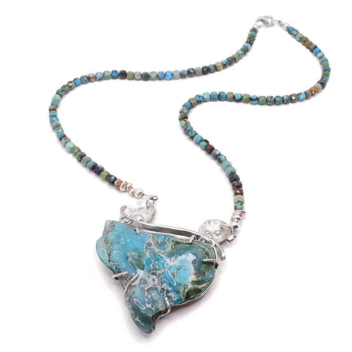 This chrysocolla necklace has a triangular-shaped light blue chrysocolla as the statement piece with silver adornments attached. The necklace is made of turquoise with varying colours of blue and green.
