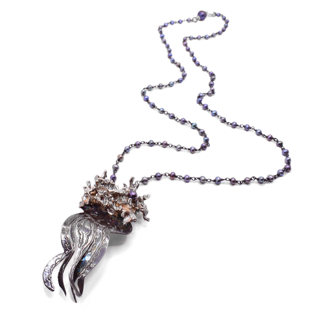 Image of jellyfish necklace laying down showing the long chain of small, purple pearls all throughout the silver chain.