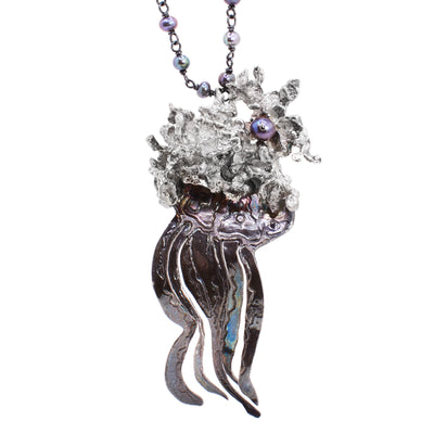 This jellyfish necklace depicts a jellyfish as the centerpiece with assymetrical tentacles. The top half of the jellyfish is in an abstract shape and has a single pearl on the side.