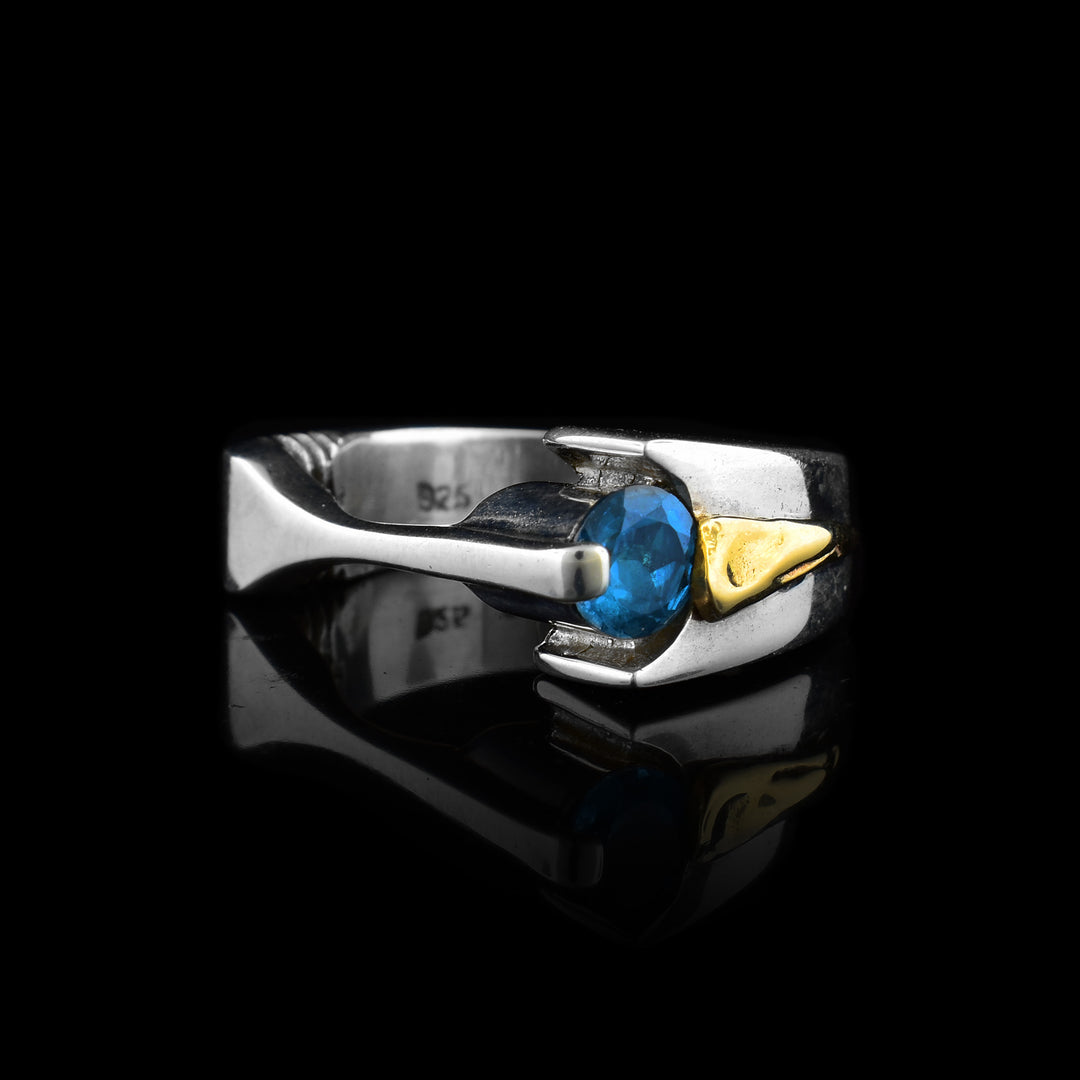 This sterling silver ring has a thin, flat part of the band in the front. There is a blue topaz gem on the side. There is a yellow gold part on the band going around the finger.