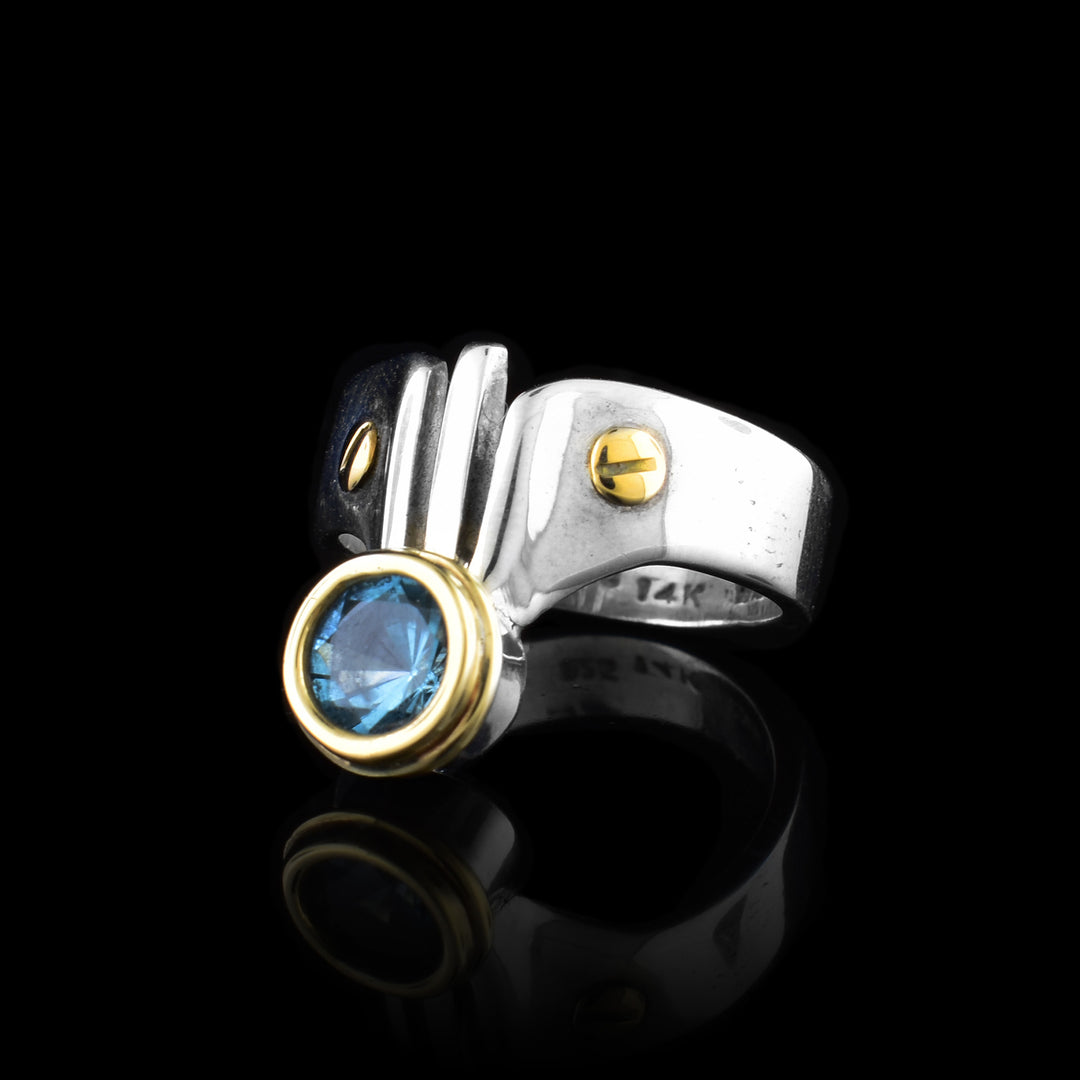 The top of this sterling silver blue topaz rings is triangular shaped and has 14K gold studs and a blue topaz gemstone.