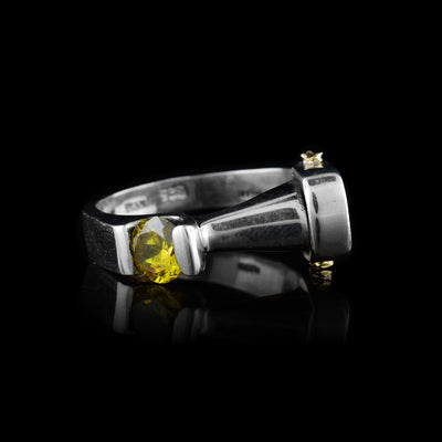 This yellow topaz ring is made from sterling silver and has an abstract design. At the top, there is a horizontal cone that attaches to the gem with is off to the left side of the band. There are two gold studs at the base of the cone.