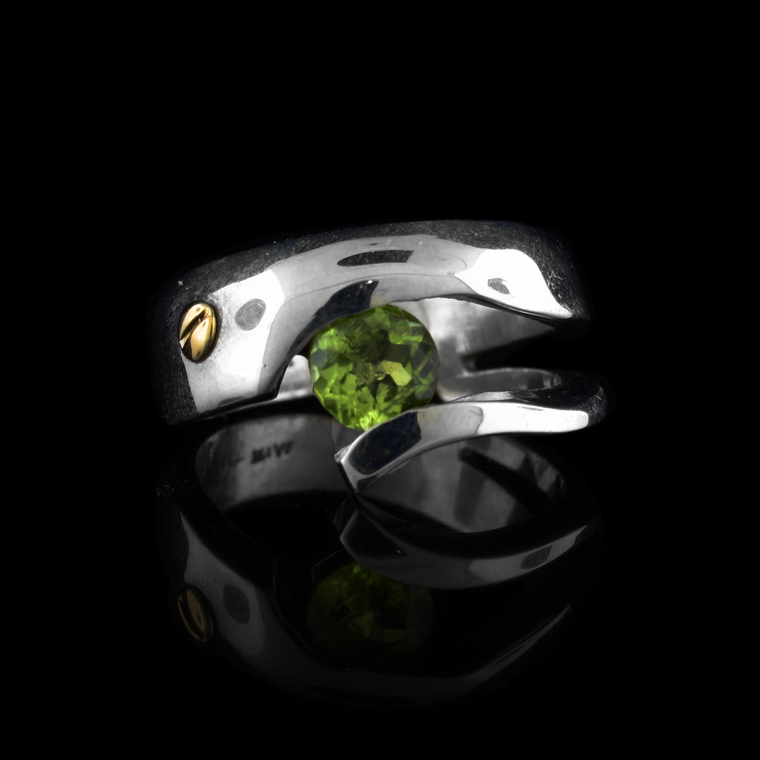 This sterling silver peridot ring has a wide band that splits at the top to hold a peridot gemstone. There is also a 14K gold stud at the top of the ring.