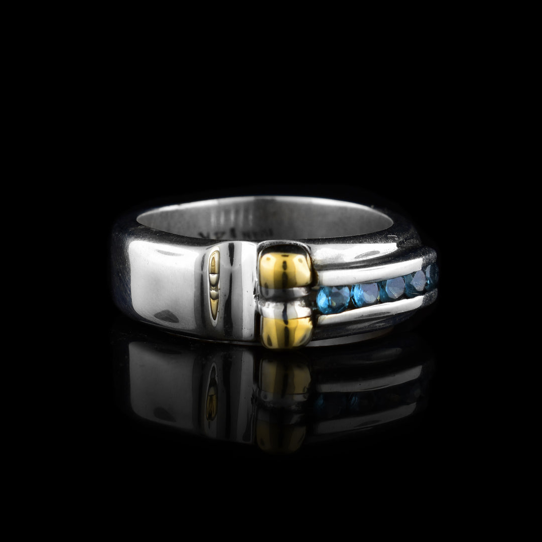 An abstract shaped silver band with five small round blue topaz stones and a 14K gold detail.