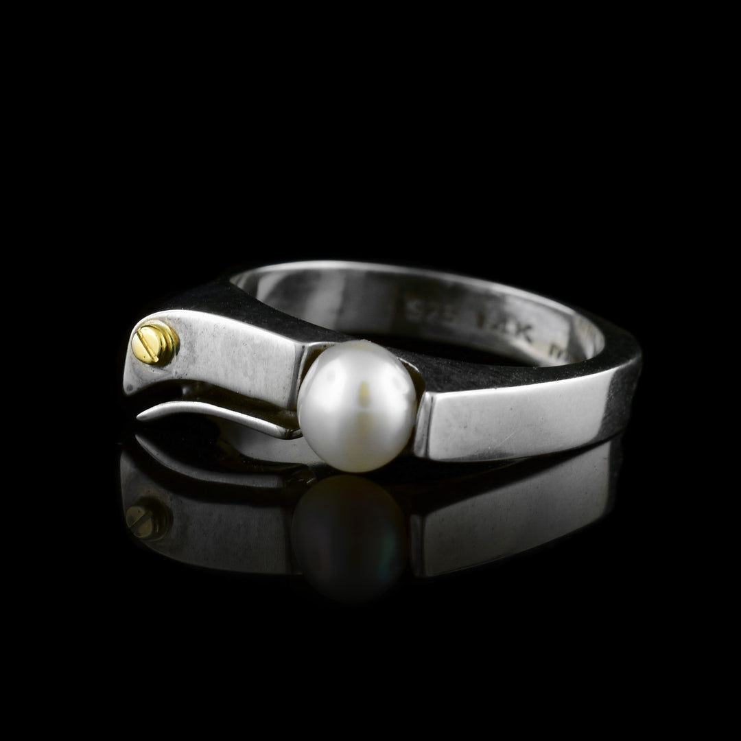 This dainty pearl ring has a sterling silver band with a thin, curved signet at the top. To one side there is a white, freshwater pearl and across from is is a 14K gold stud.