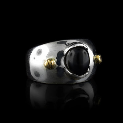 This wide band solitaire ring is made from sterling silver and has a side band that tapers slightly in the back. There is a large, oval shaped black onyx gem in the center with 14K gold studs to either side of it.