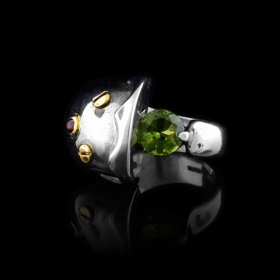 A sterling silver band that is split in the middle. There is a round peridot gemstone in the middle of the split. One of the split sides is bigger than the other, and has three gold, round details.