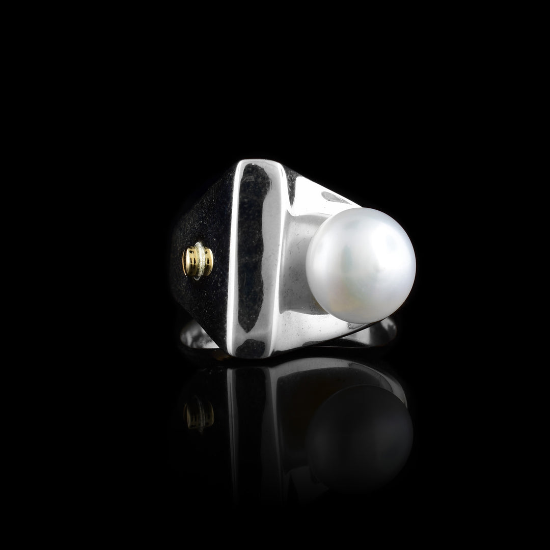 This sterling silver signet ring comes to a soft point at the top of the ring. On the sides of the signet are a fresh water pearl and a garnet gem wrapped in 14K gold.