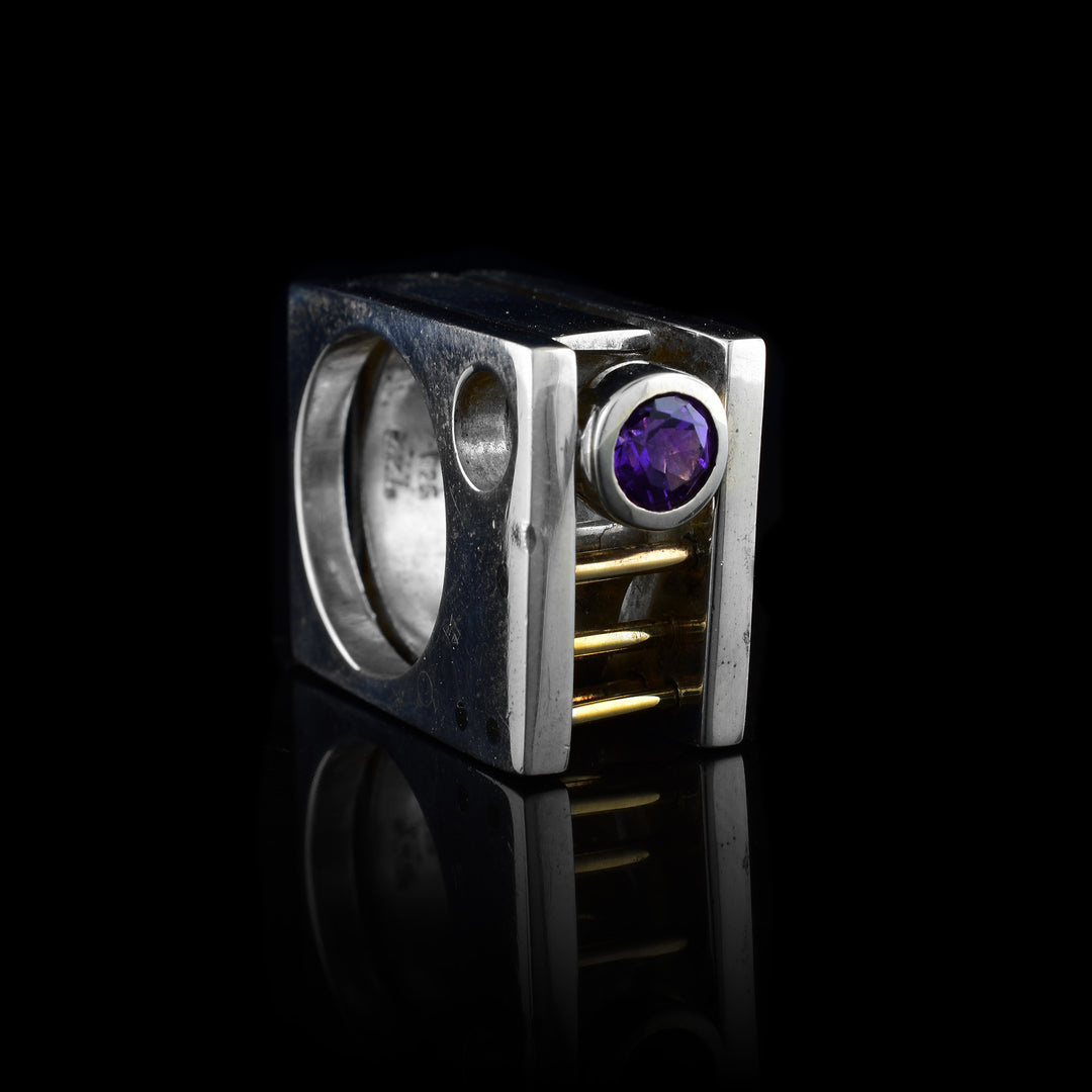This abstract, square ring has three sterling silver layers with an amethyst gemstone between them. By the gemstone, there are three 14K gold rods running through two bands. The entire ring is square shaped.