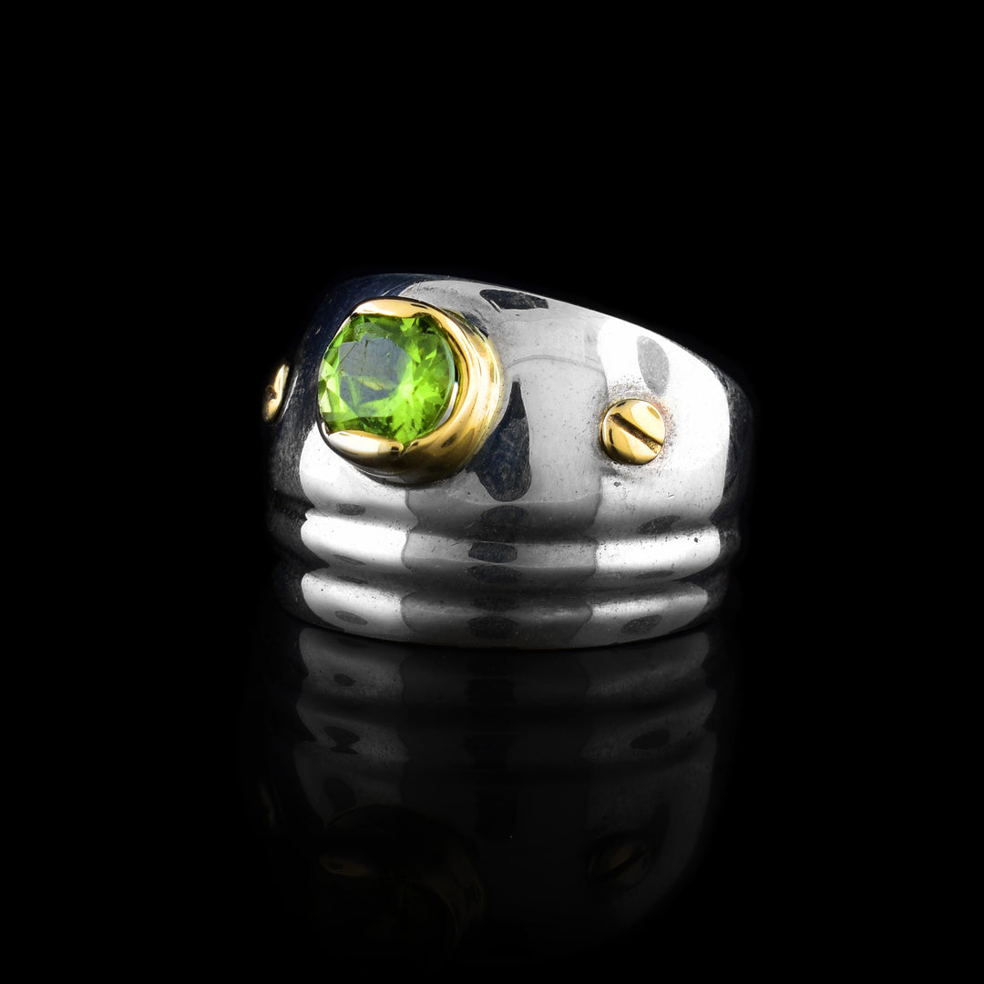 This sterling silver and gold ring has a wide, tapered band. On it is a peridot gemstone surrounded by 14K gold with gold studs on both side of the gem.