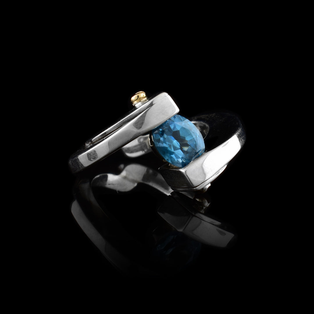 This abstract sterling silver and gold ring has two half circle pieces attached at the bottom of the ring. At the top of the ring, between the two pieces is a topaz gemstone with two 14K gold studs.