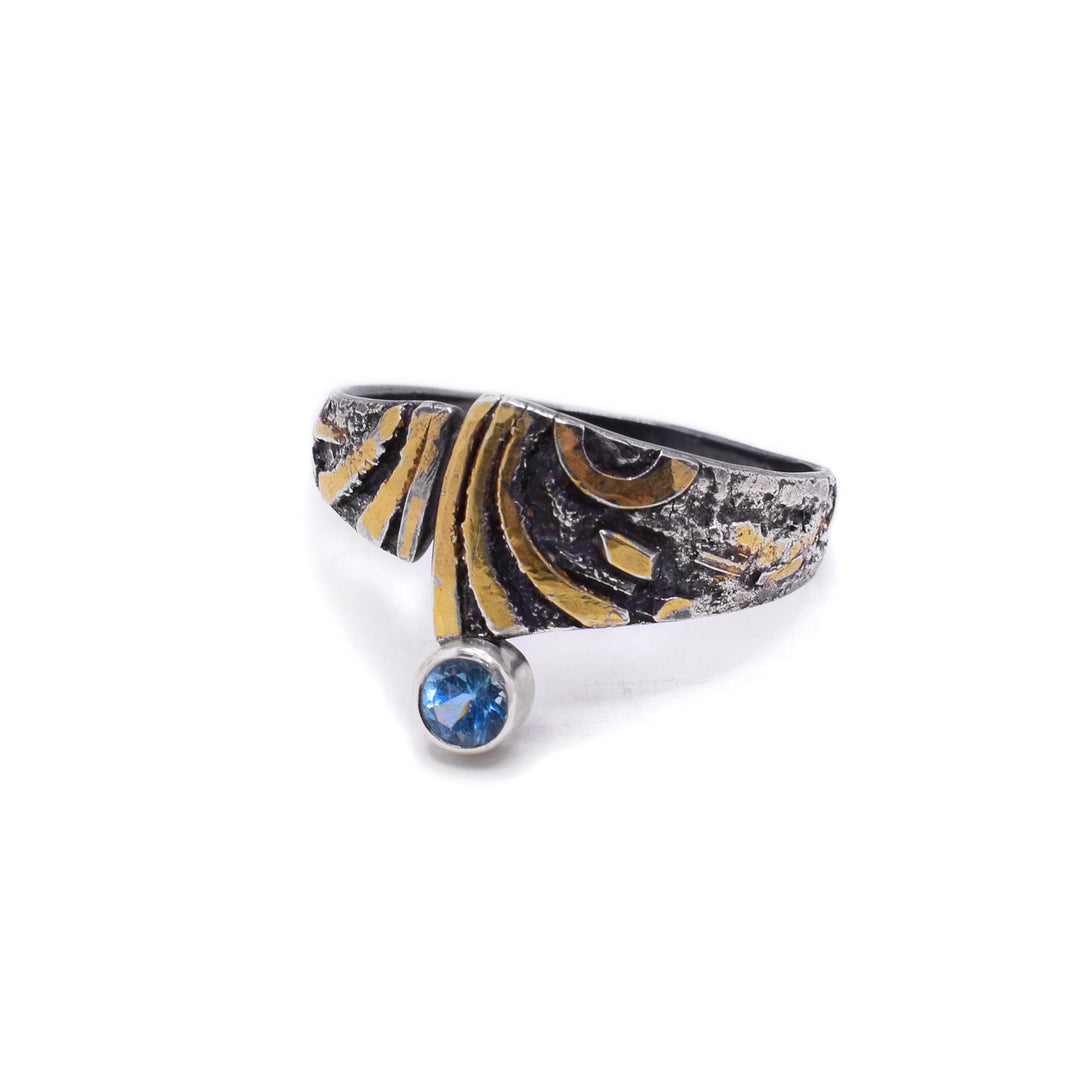 This dainty apatite ring has gold accents in varying shapes across the front of the ring and the circular apatite gemstone is encased in a silver holding at the bottom of the center of the ring.