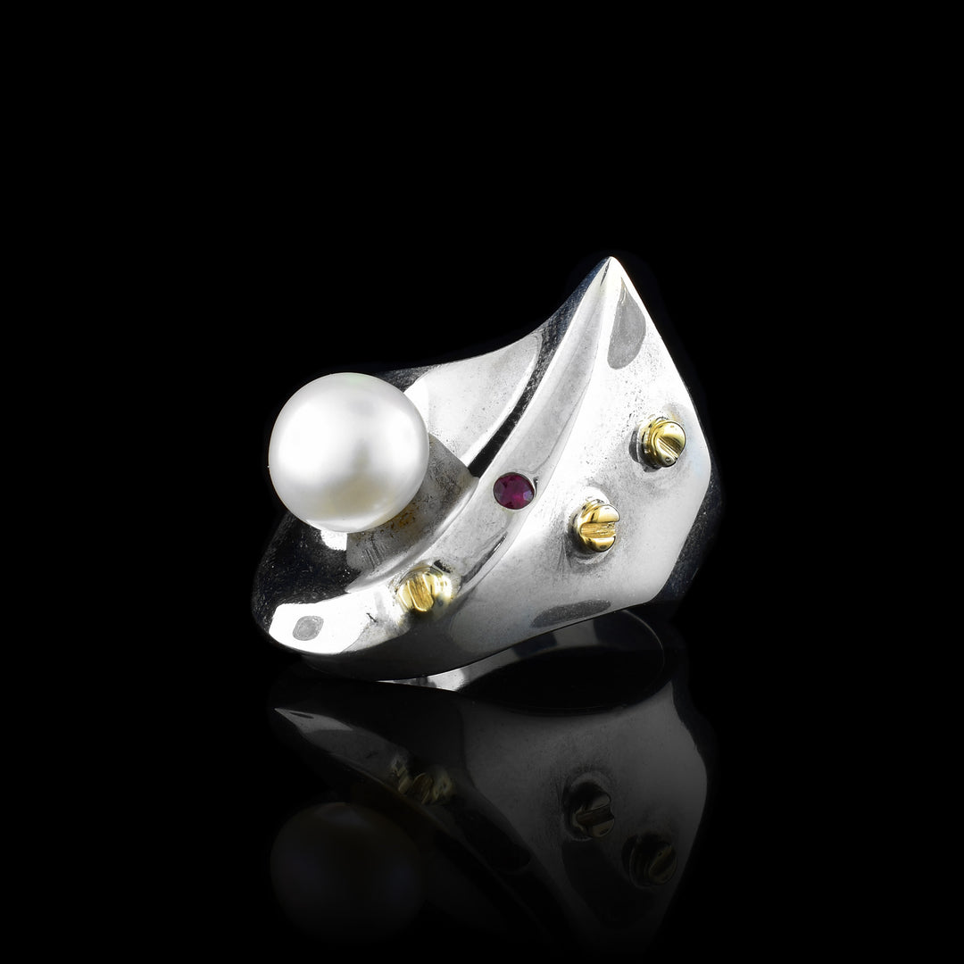This sterling silver signet ring has a curved signet that comes to a point. There is a freshwater pearl, garnet gem and 14K gold studs on the signet.
