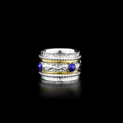 This brilliant spinner ring had a wide sterling silver band that has intricate designs made across the surface of it. In the middle of the band there is a thin, carved band with four lapis lazuli gems embossed into it, this part of the piec can be spun around the band. on both sides of the spinning band are brass wires and bead designed silver wires. The ends of the main band flare out at the ends.