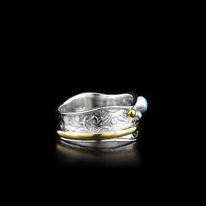 This spinner ring is made from sterling silver, brass and turquoise gemstones. There is a wavy silver band with a turquoise gem and brass beads on the surface of it. There is a brass hoop on the band that can be spun around the piece.