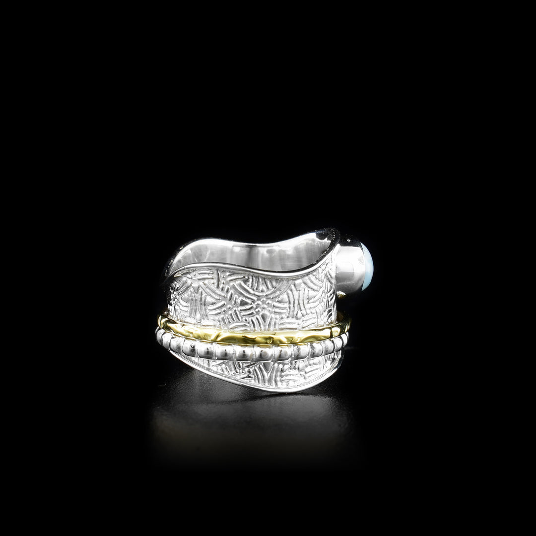 This spinner ring is made form sterling silver, brass and larimar gemstone. There is a wide, wavy and silver band with an ovoid larimar gem held on the top of it, There is a textured silver hoop and a brass hoop on the band that spin around the band.