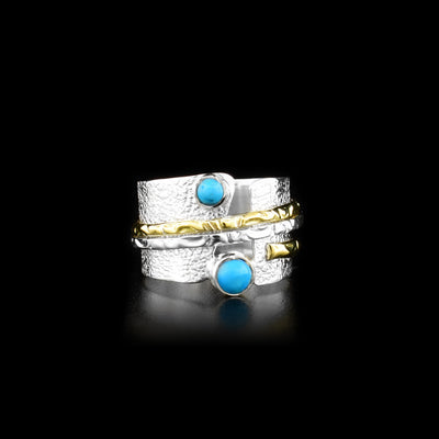 This stunning spinner ring has a wide sterling silver band with a textured surface and two small, round turquoise gems embossed onto either end of the bands width. There are ribbed textures on a silver and a brass ring that is wrapped around the band. These textures rings can be spun around the band.