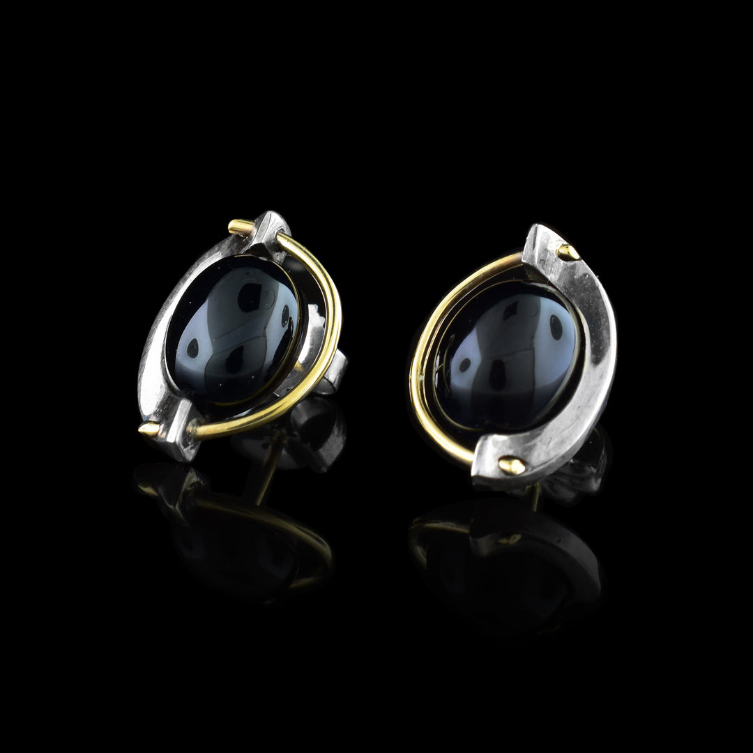 These black onyx earrings have sterling silver cradles holding round black onyx gems. There is also a 14K gold wire running around the gem. 