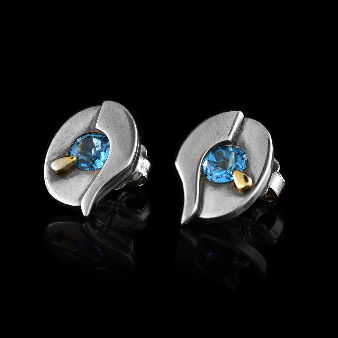 These sterling silver topaz stud earrings are teardrop shaped and have a topaz gem embedded in the middle of each earring. Beside each gem is a decorative 14K gold stud.