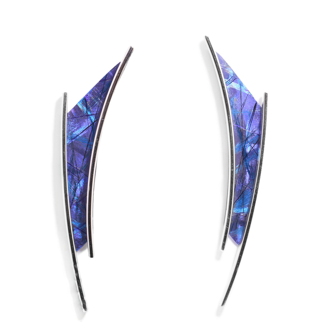These funky, long stud earrings have long, thin sterling silver wires that frame a thin, trapezoid shaped piece a titanium between them. There are blue and purple designs on the titanium and the wires extend past the pieces.