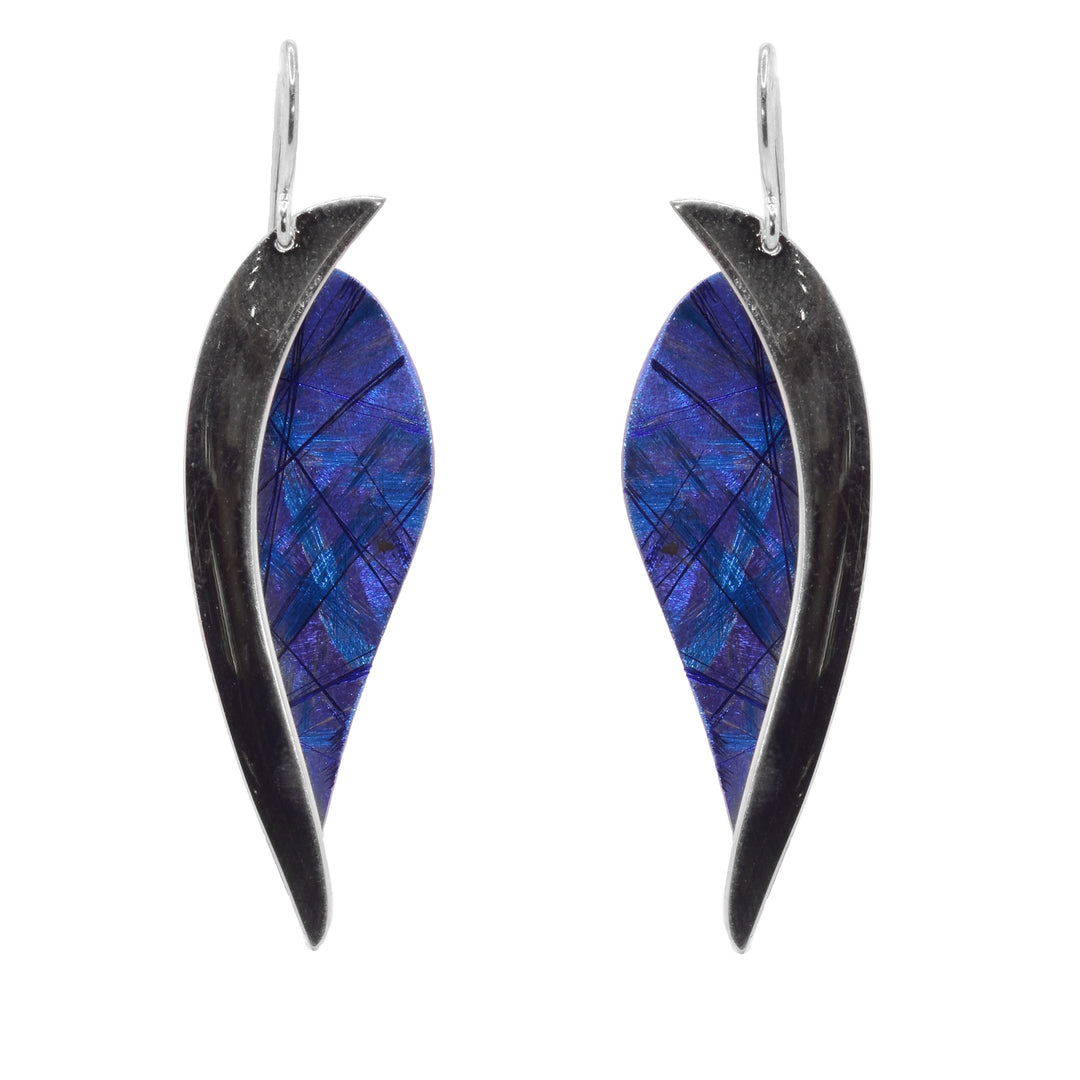 These titanium dangle earrings have leaf shaped pieces of titanium with blue and purple line designs. There is a wide, curved sterling silver band running down the side of the hangs.