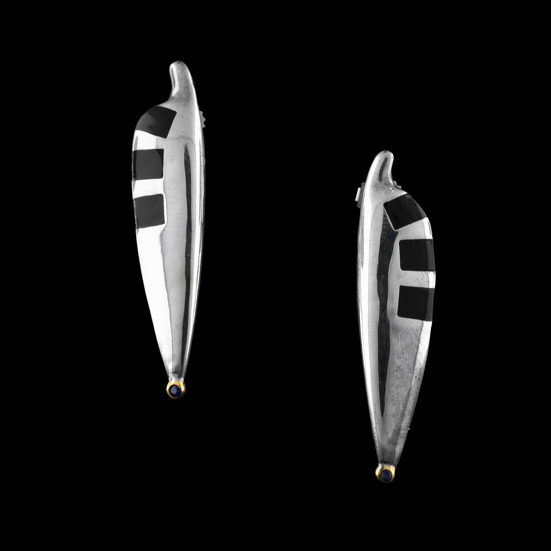 These sterling silver sapphire earrings are wide and vertical. There are cutouts along the earring with square pieces of plexiglass imbedded. At the bottom of the earrings are sapphires that are wrapped in 14K gold.  