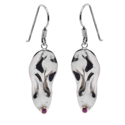 These ruby drop earrings have large, sterling silver hangs that have been shaped to have unique folds and wavy designs in them. There are small rubies that are bezel set in 14K gold at the bottom of the hangs.