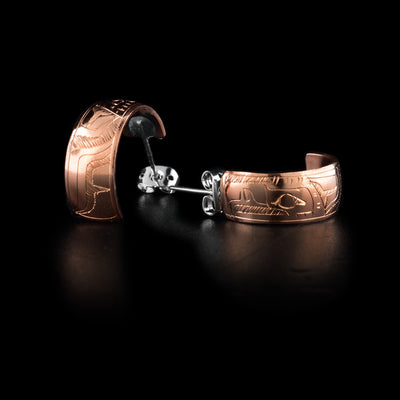 These copper hoop stud earrings have wide bands made from copper. The bands form small, half circles and there is a depiction of the Eagle's head carved into them. The beak, teeth and eyes are shown and the head is facing the studs.