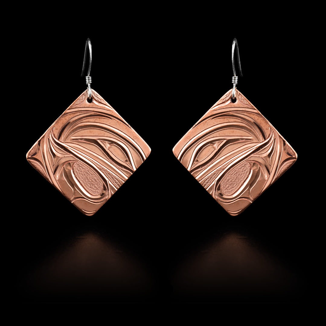 These Hummingbird dangle earrings have large hangs made from copper. The hangs are square shaped and are attached to the hooks at the corner. There are wavvy designs carved into the hangs depicting the head of the Hummingbird legend at a side profile.