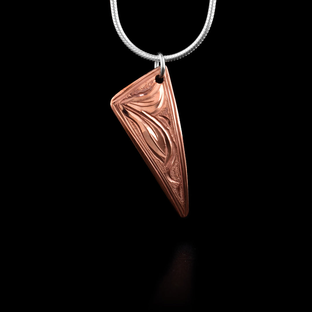 This Hummingbird pendant has an acute triangle shaped and is made from copper. There is an abstract depiction of the Hummingbird carved into the piece and dimpled textures in the negative spaces of the scene.