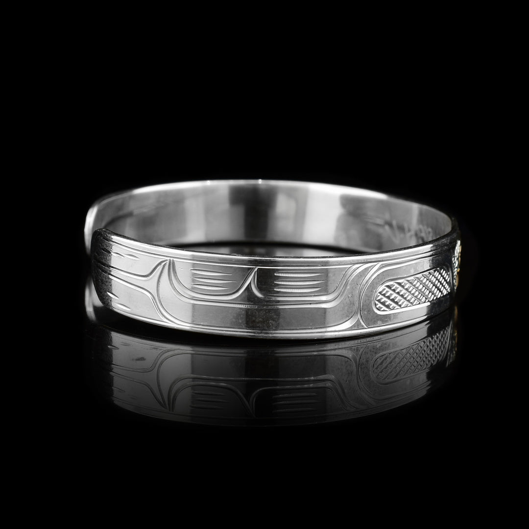 This sterling silver cuff bracelet has a single, thin band with a gap in the back. There are carvings on the surface of the band depicting the Raven and the head of it is made from 14K gold. 