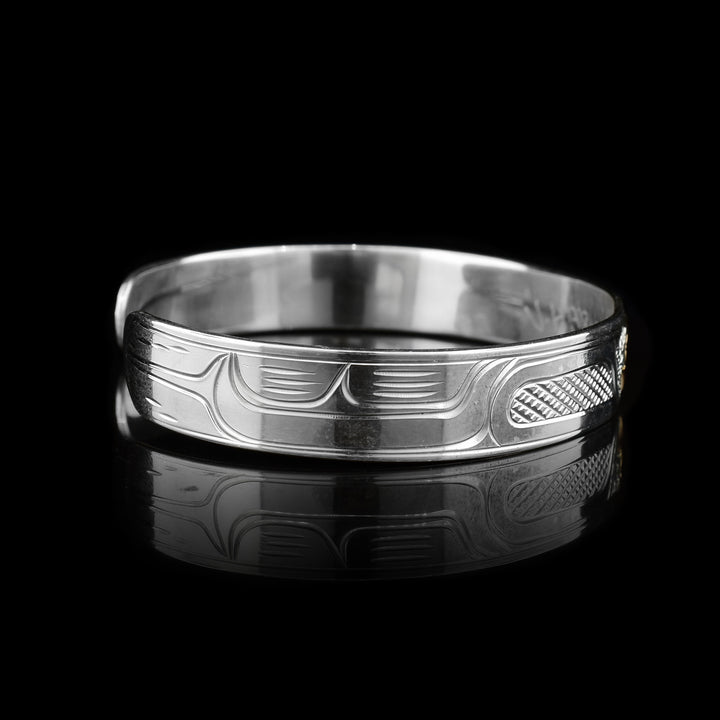 This sterling silver cuff bracelet has a single, thin band with a gap in the back. There are carvings on the surface of the band depicting the Raven and the head of it is made from 14K gold. 
