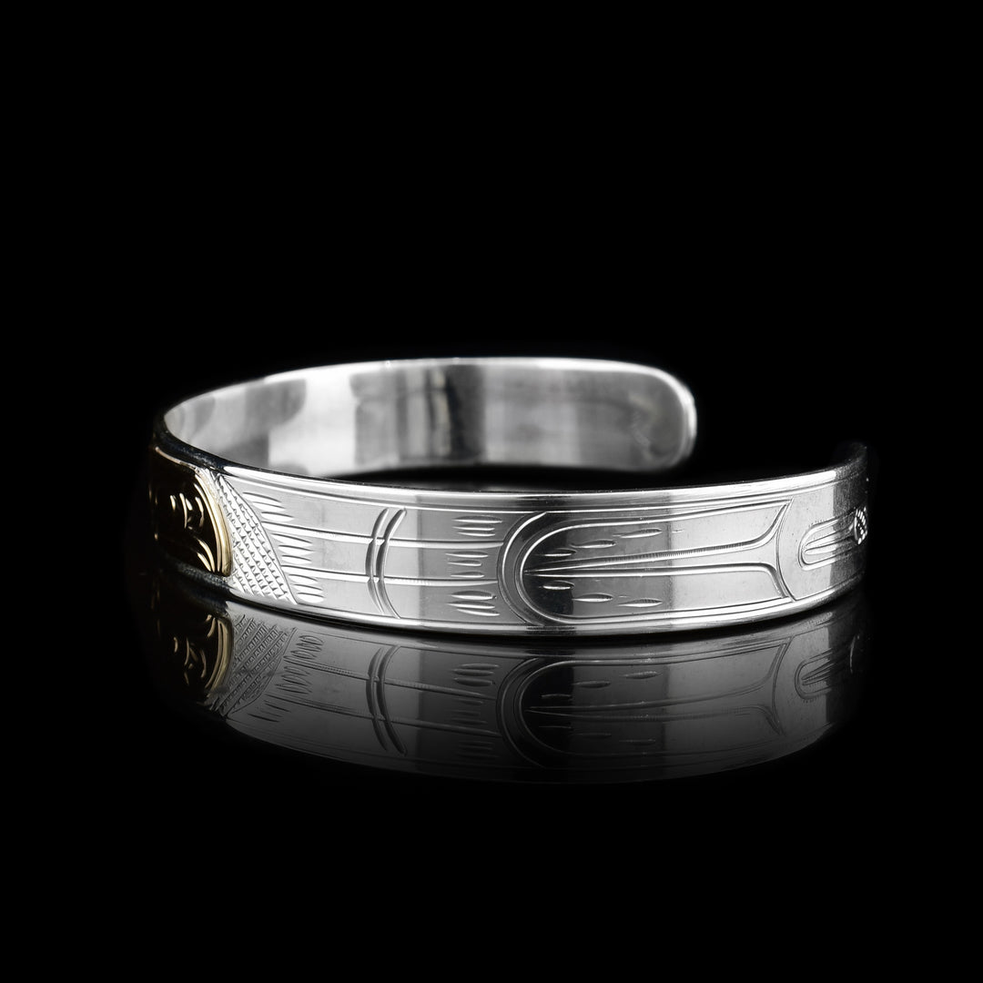 This sterling silver cuff bracelet has a single, thin band with a gap in the back. There are carvings on the surface of the band depicting the Raven and the head of it is made from 14K gold. 