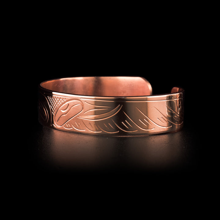This Hummingbird cuff bracelet has a single band with a gap in the back and is made from copper. There is a depiction of the head of the Hummingbird carved at a side profile into the band. The beak is facing a flower on one end and on the other its wing is seen out stretched. There are cross hatching designs in the background of the scene.