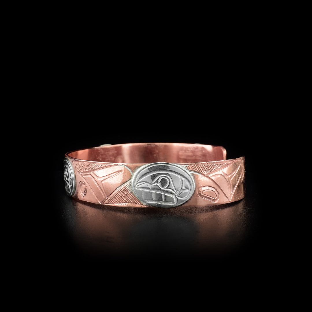 This copper cuff bracelet has three depictions of the Orca carved around its band. The heads of the Orcas are made from sterling silver.