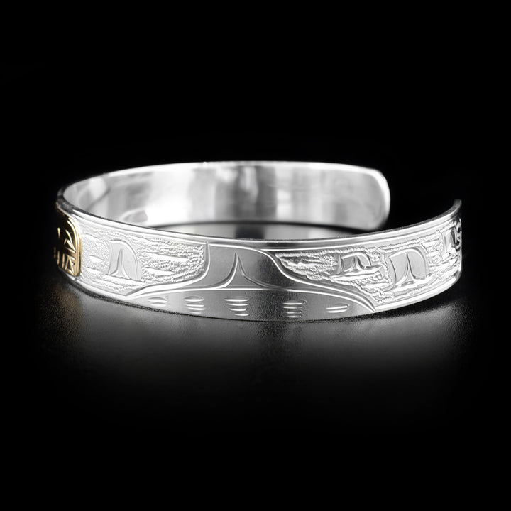 Right angle photo of the bracelet shows lots of fins peaking out of the water signifying an orca pod. The background is stippled.