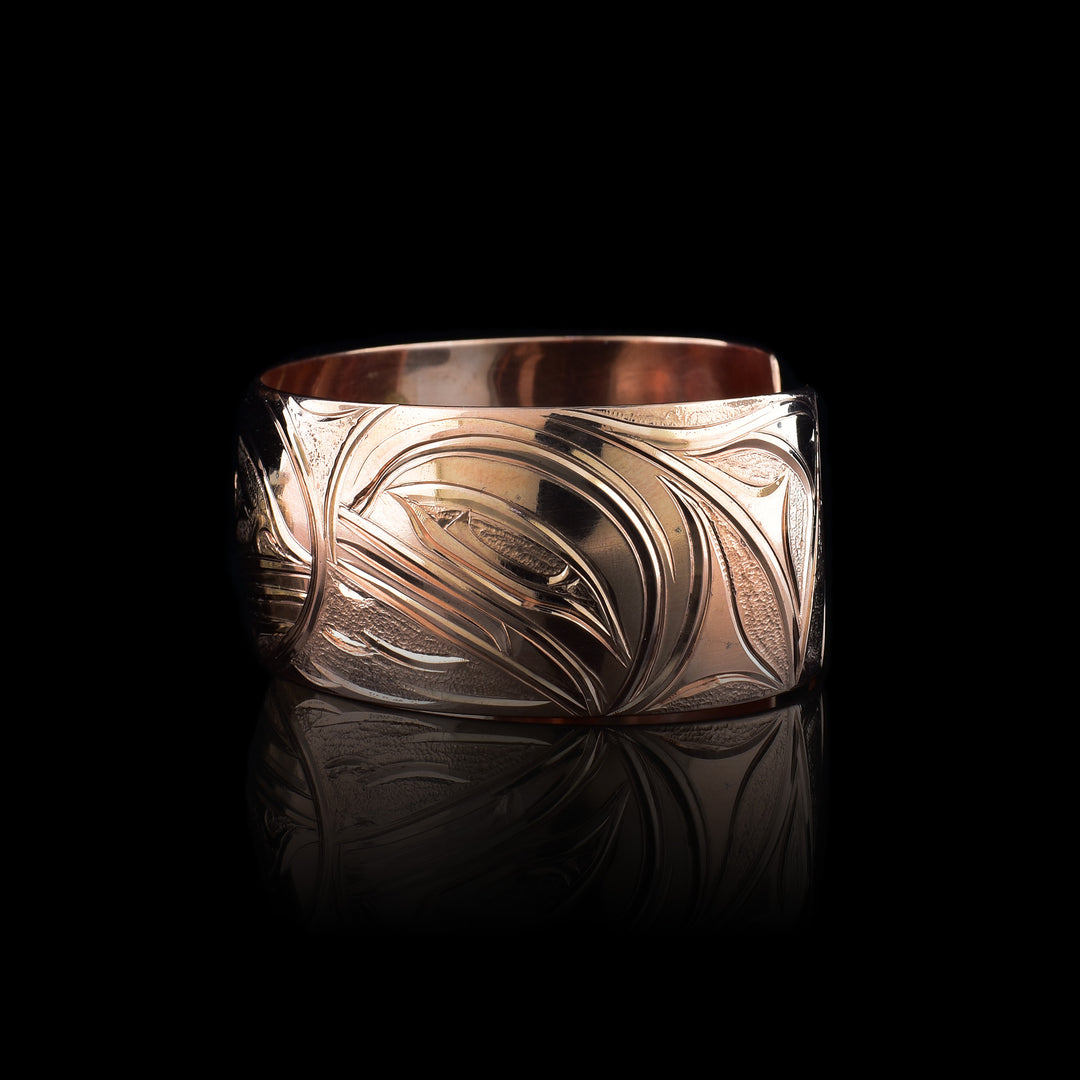 This copper cuff bracelet has a single, side band with a gap in the back. There is a baby Orca depicted in the womb with its mother watching over is on one side of the piece and a two dorsal fins in the ocean depicted on the other side. This piece represents family and community.