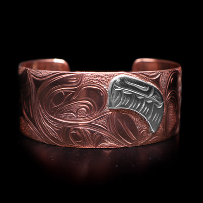 This Eagle bracelet has a wide band made from copper and with a gap in the back. There is a depiction of a baby eagle with its wing made from sterling silver being watched over by its mother carved into the band.