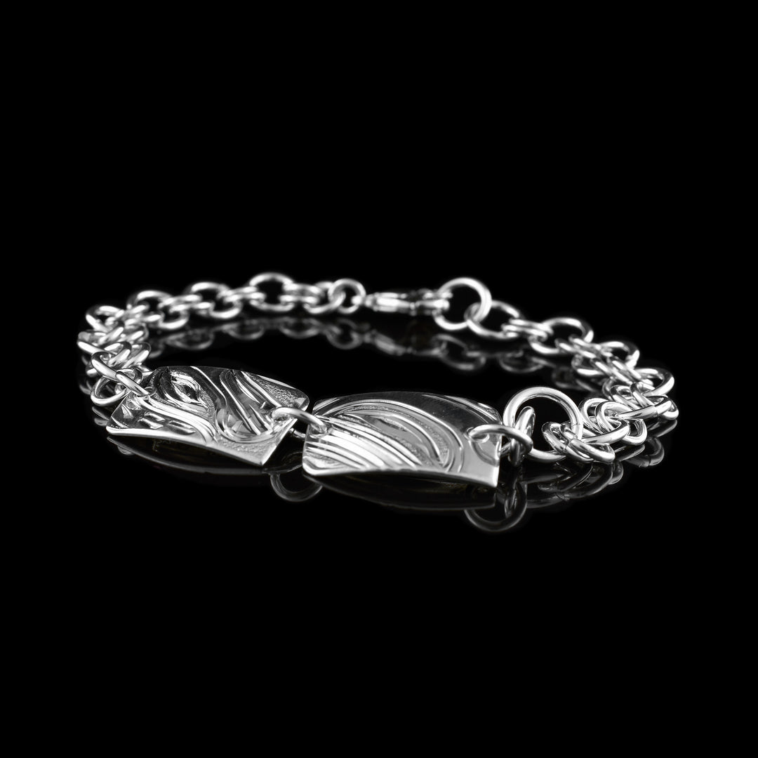 This sterling silver chain bracelet has double silver links hooped each other to make the chain. There are two, rectangle plates at the top of the piece with the head of the Bear and Orca carved into them at a side profile.