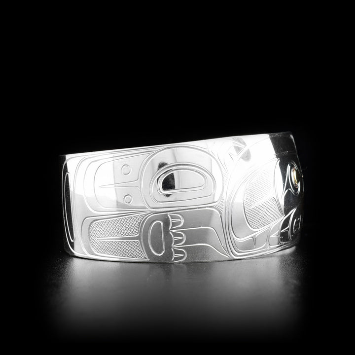 This silver and gold bracelet is made from sterling silver and 14K gold and has a wide band that tapers slightly. There is a depiction of the Bear carved into the surface of the band and the eye of the Bear is made from 14K gold.