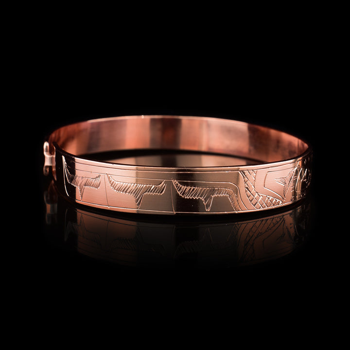 This copper bangle bracelet has a single, thin band with a simple hook clasp in the back. There is a depiction of the Hummingbird and the Eagle that have been beautifully carved into the surface of the band. The heads of the legends meet and are facing each other at the top f the band.