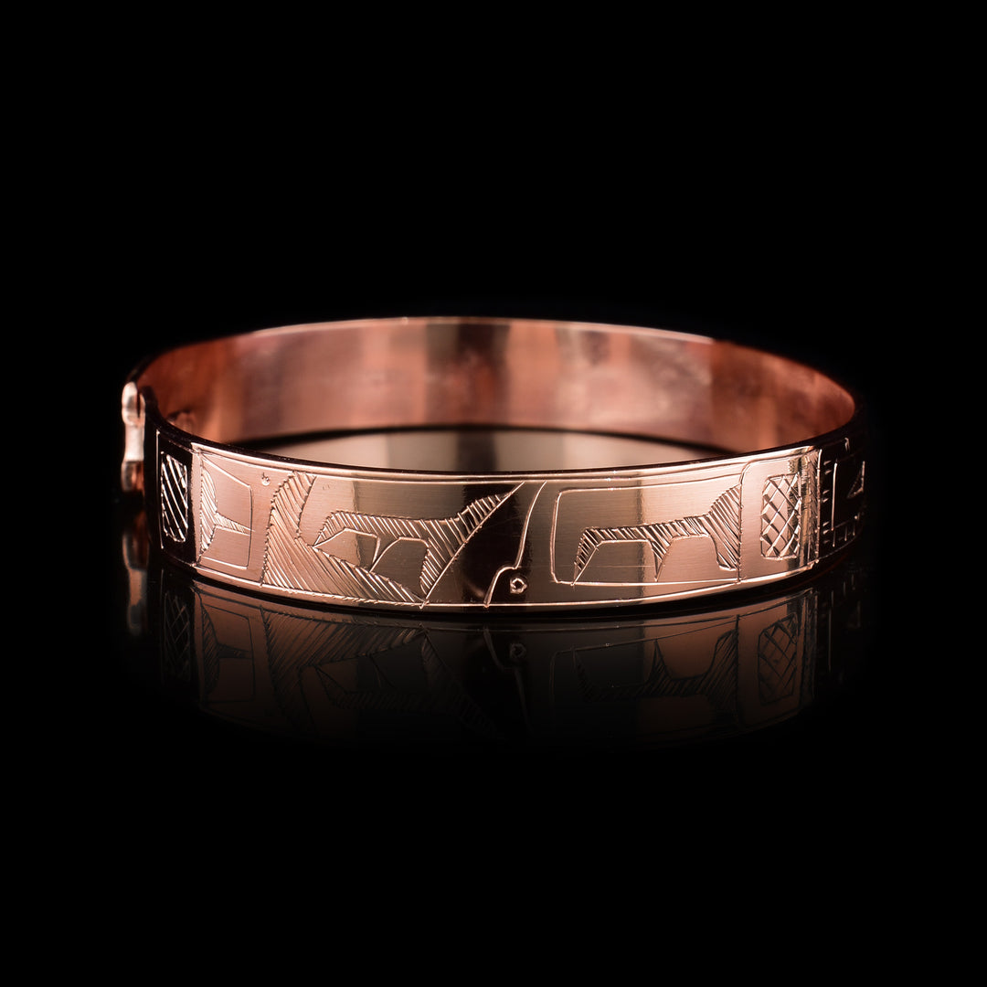 This copper bangle bracelet has a single, thin band with a simple hook clasp in the back. There is a depiction of the Orca and the Eagle that have been beautifully carved into the surface of the band. The heads of the legends meet and are facing each other at the top of the band.