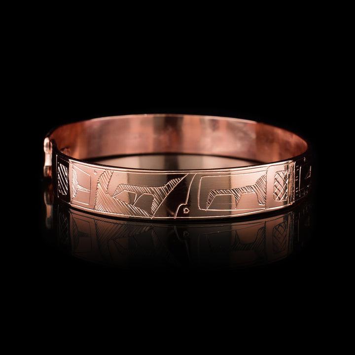 This copper bangle bracelet has a single, thin band with a simple hook clasp in the back. There is a depiction of the Orca and the Eagle that have been beautifully carved into the surface of the band. The heads of the legends meet and are facing each other at the top of the band.
