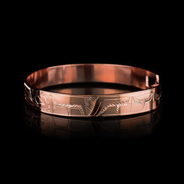 This copper bangle bracelet has a single, thin band with a simple hook clasp in the back. There is a depiction of the Raven and the Eagle that have been beautifully carved into the surface of the band. The heads of the legends meet and are facing each other at the top of the band.