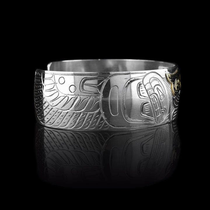 This silver and gold cuff bracelet has a single, wide band with a depiction of the Heron with outstretched wings carved into the surface of the piece. The head of the legend is made in 14K gold.