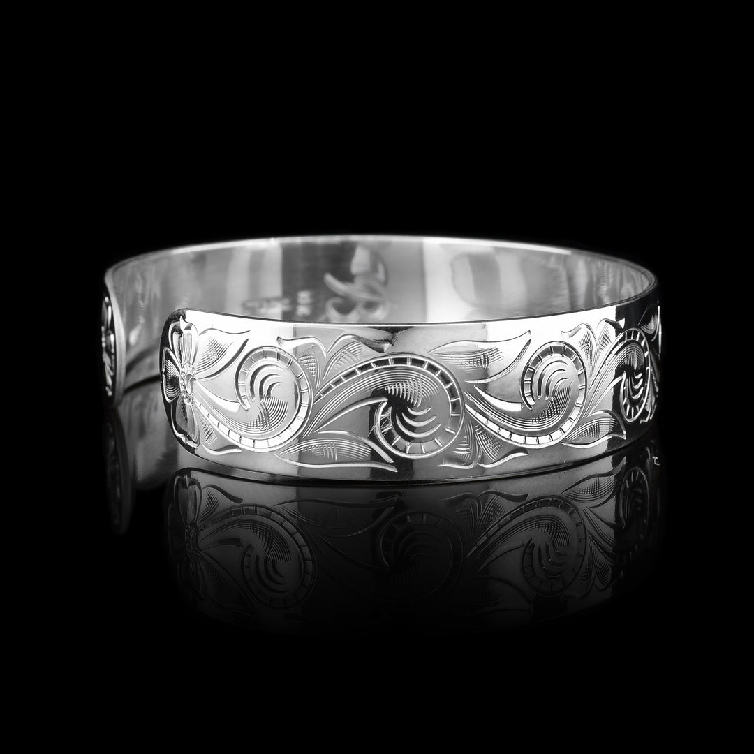 This sterling silver bracelet cuff has a wide band with carvings depicting designs across the band and a bear. The bear is made of 10K gold.